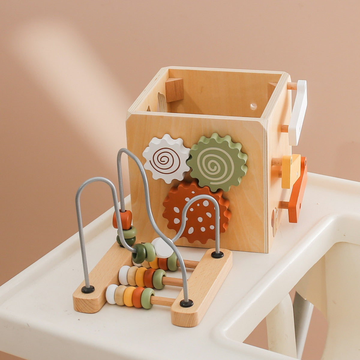 Wooden activity cube with bead maze on a white table